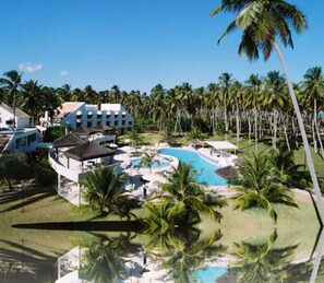 Ein Resort mit einem zentralen Pool, umgeben von Palmen und einem Gebäude mit mehreren Balkonen.