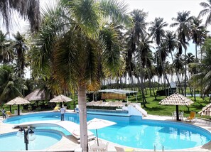 A swimming pool with lounge chairs and umbrellas, surrounded by palm trees. - Hotel D'Anatureza (Maceió)