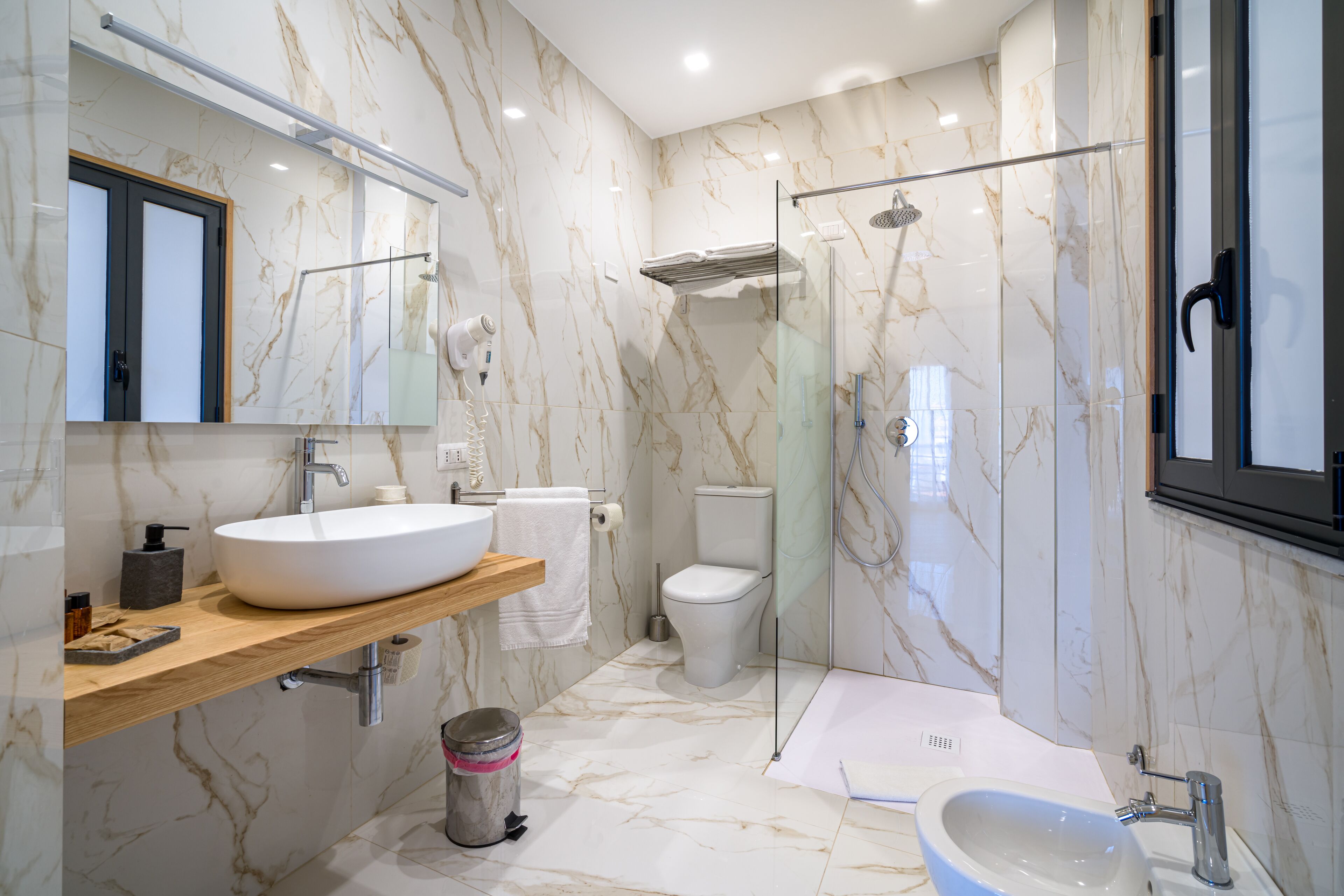 Ein modernes Badezimmer mit einem großen, weißen Waschbecken, einer Duschkabine aus Glas und Marmorwänden.