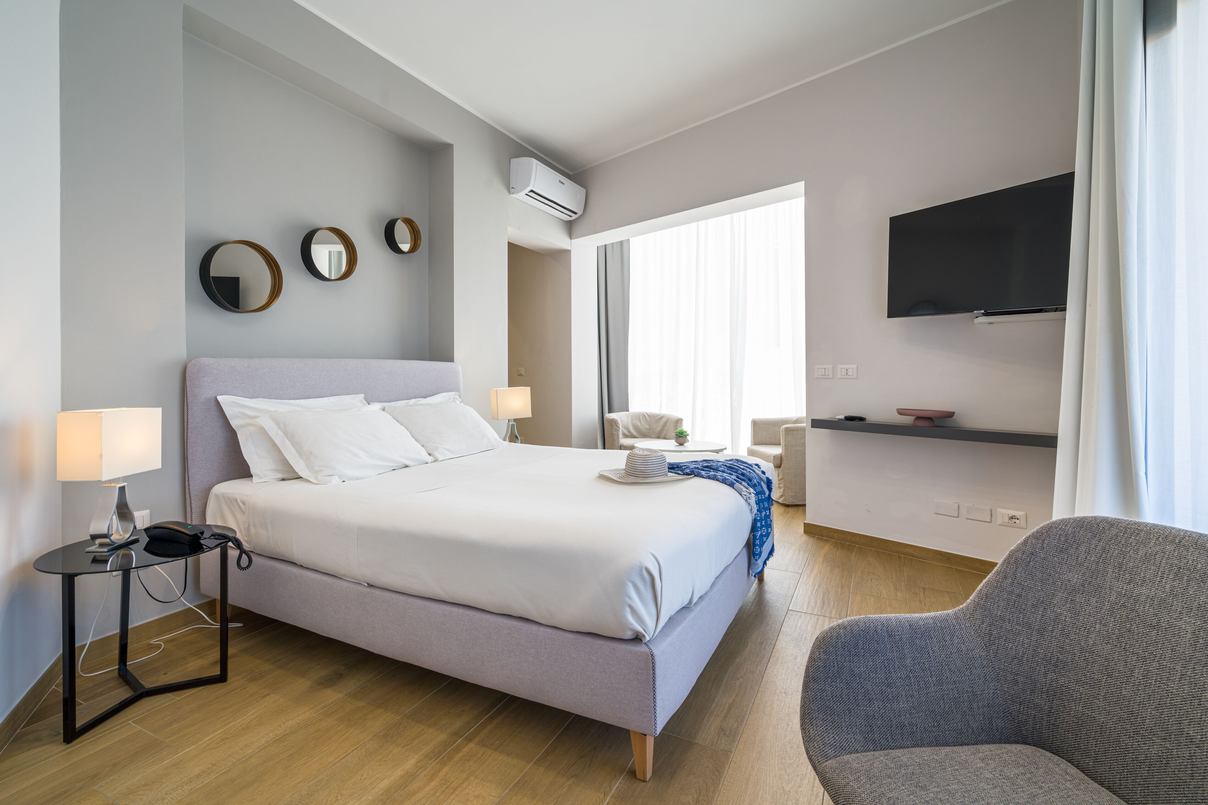 A modern hotel room with a bed, bedside table, lamp, and a TV mounted on the wall.