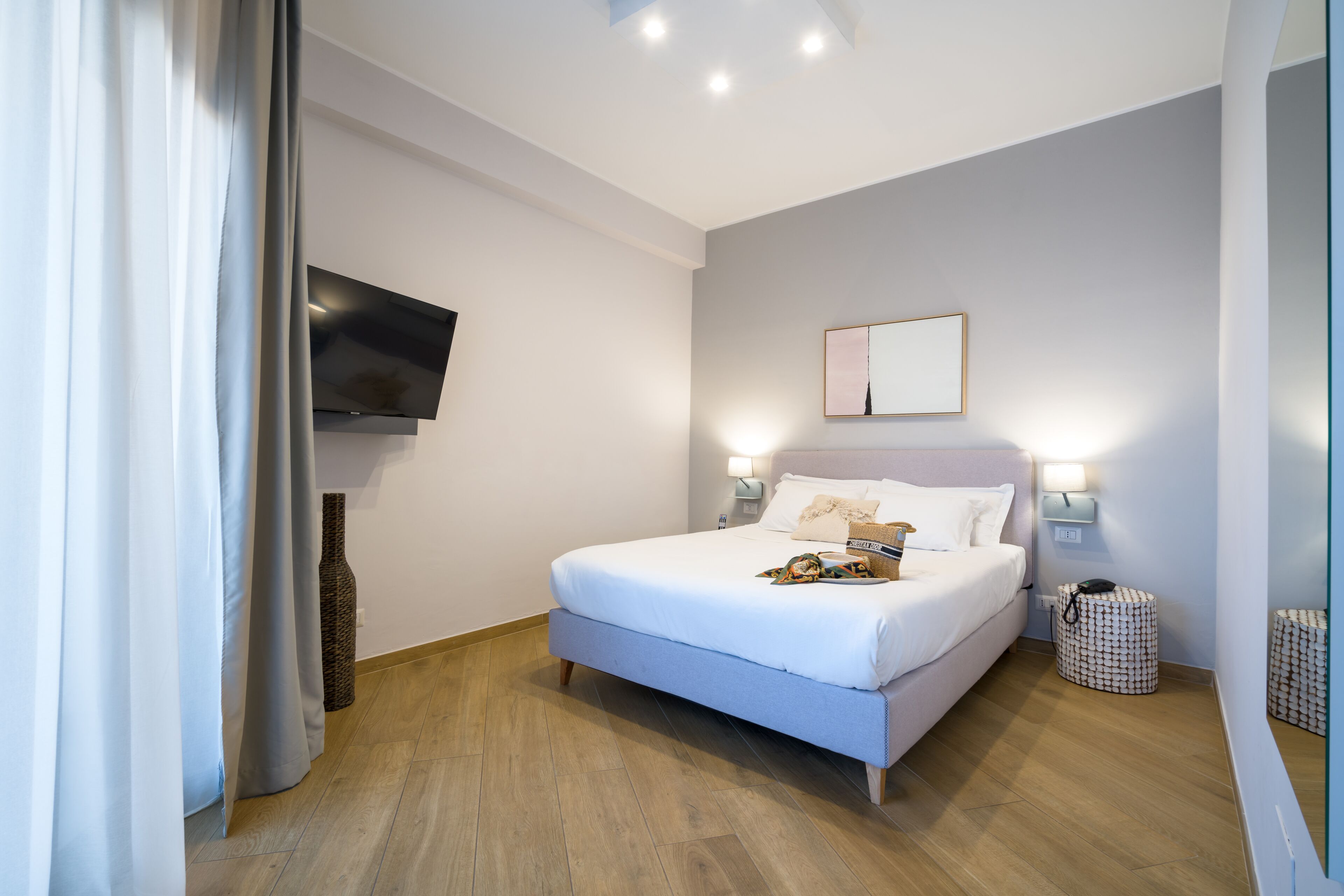 Ein modernes Schlafzimmer mit Bett, Nachttischlampen, einem Flachbildfernseher und einem kleinen Beistelltisch.