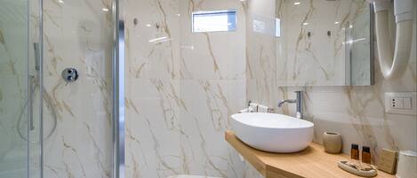 A modern bathroom with a glass-enclosed shower, a marble-tiled wall, a wooden vanity with a white sink, and a handheld showerhead.