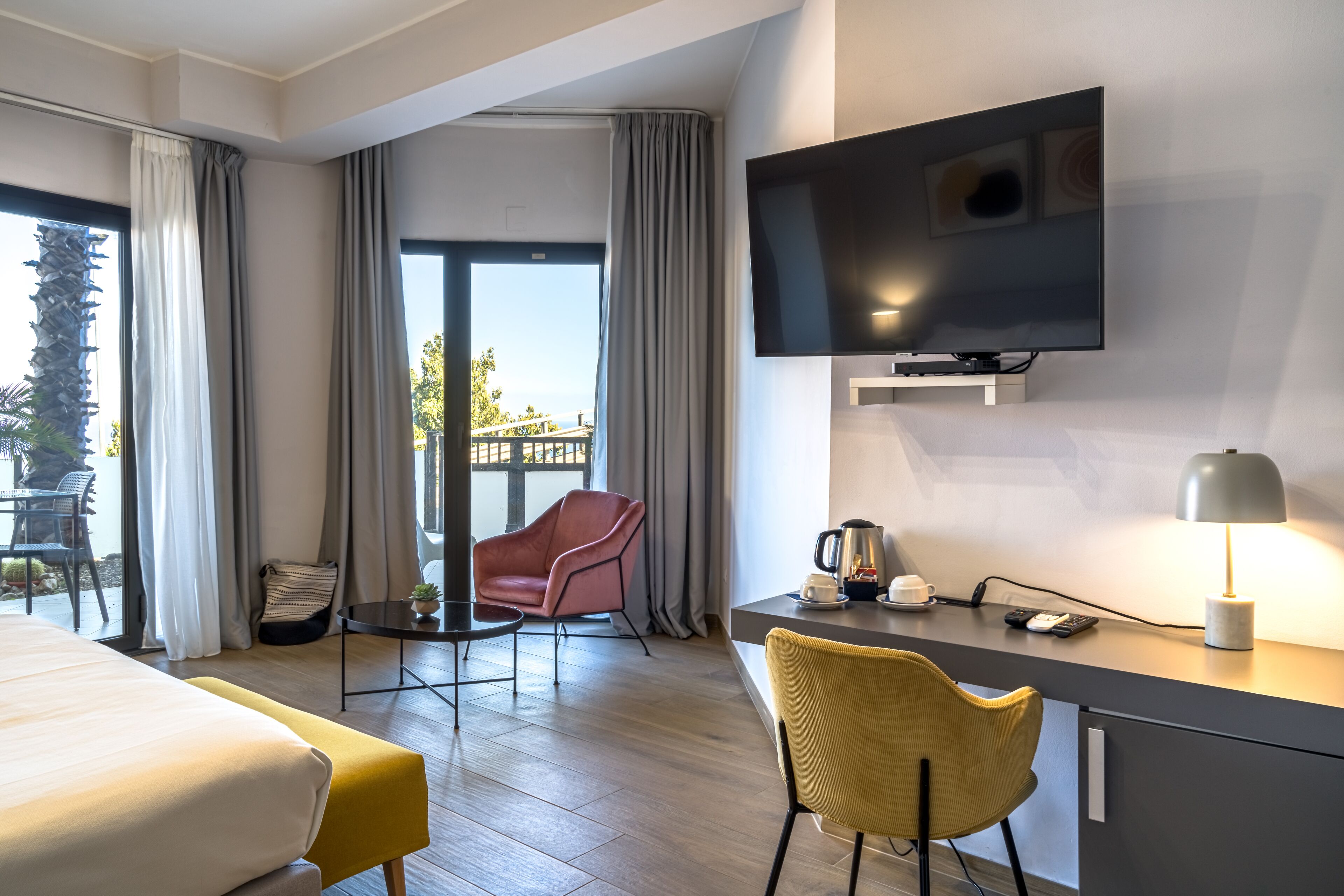 A modern hotel room with a bed, a desk with a lamp, a TV, and a chair.