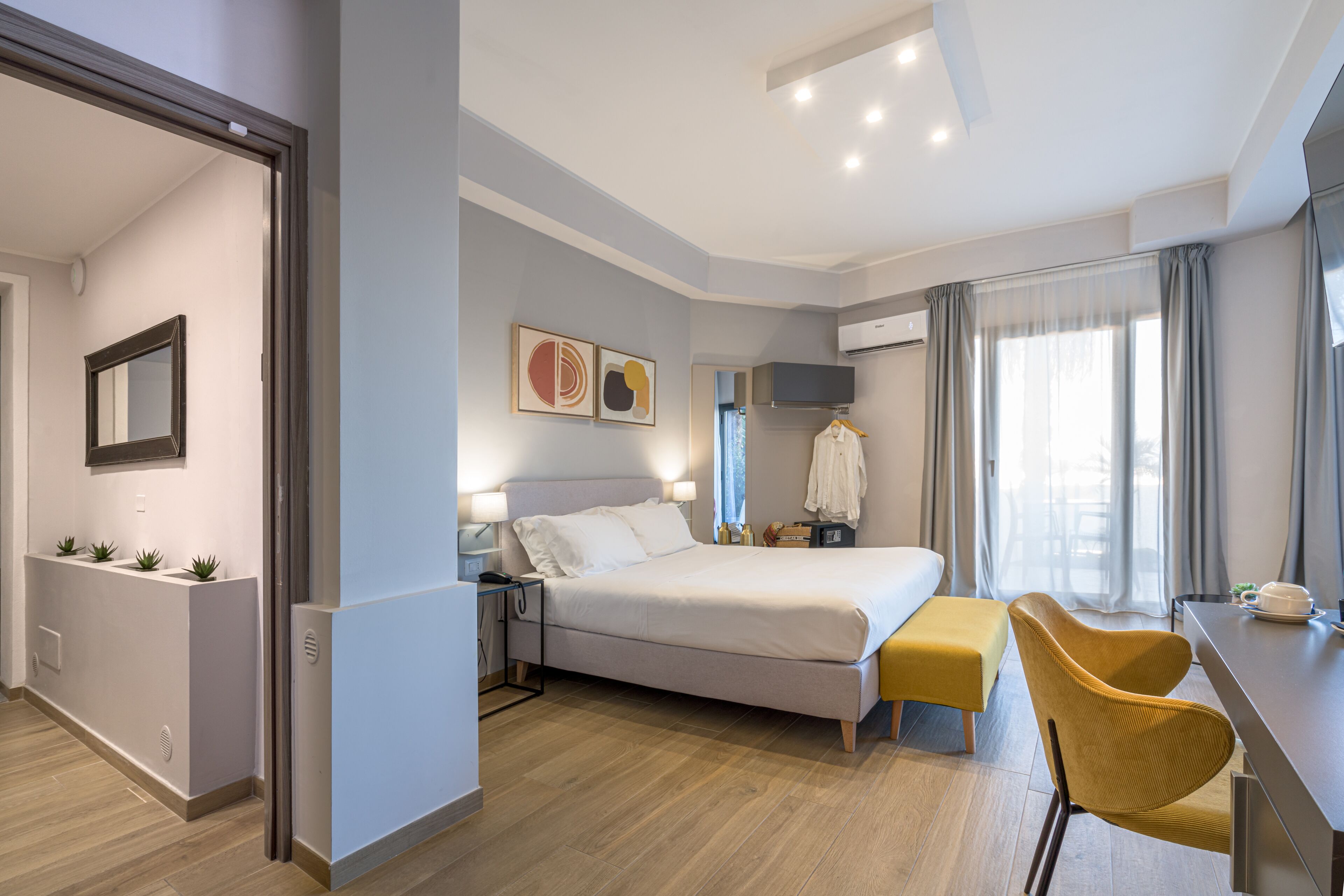 A modern hotel room with a bed, bedside table, lamp, and a desk with a chair.