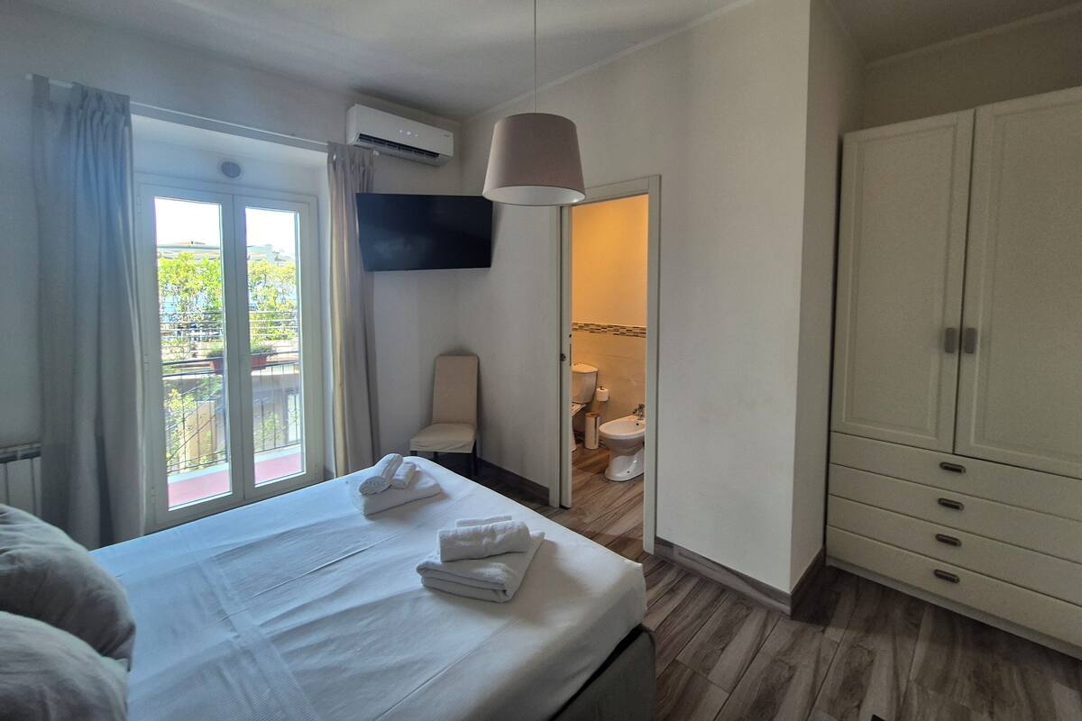 A hotel room with a bed, a TV mounted on the wall, a wardrobe, and a bathroom visible through an open door.