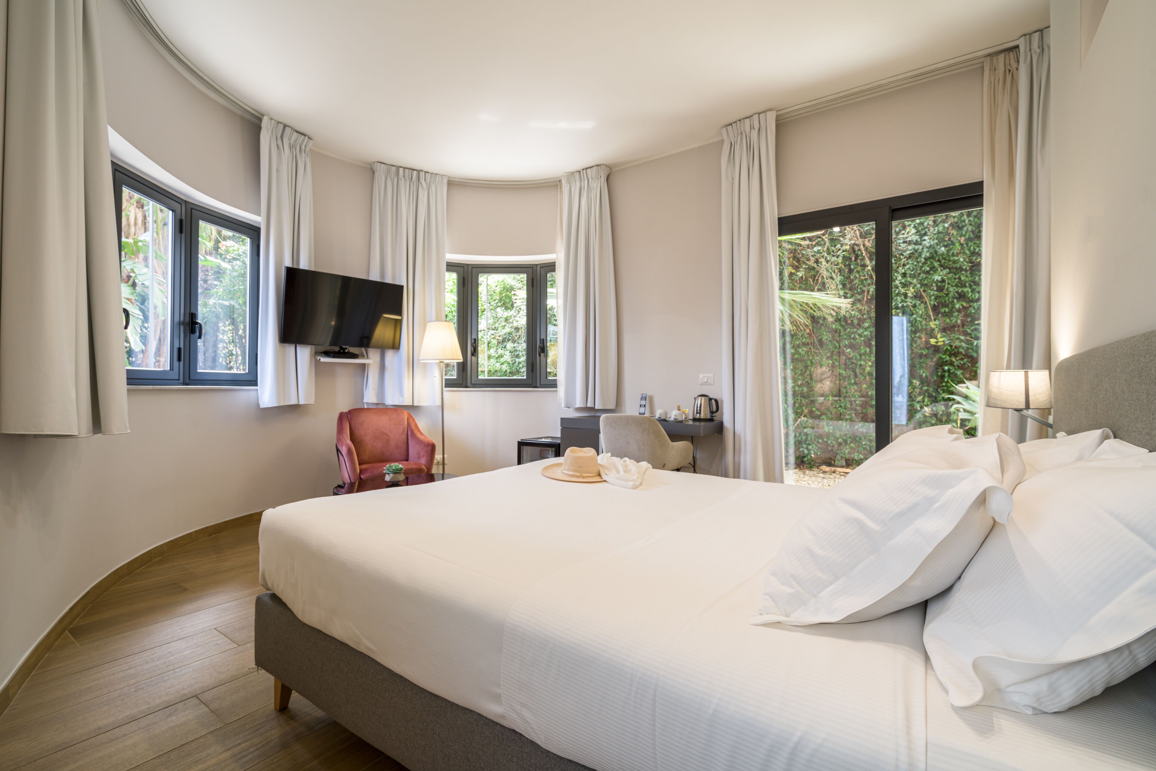 Ein Hotelzimmer mit einem großen Bett, einem an der Wand befestigten Fernseher, einem Schreibtisch mit Stuhl und Fenstern mit Vorhängen.