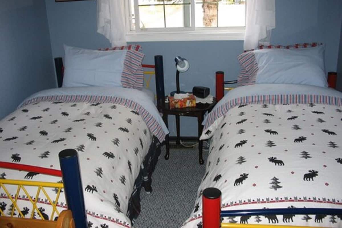 A bedroom with two beds, a nightstand, a window with curtains, and a painting on the wall.
