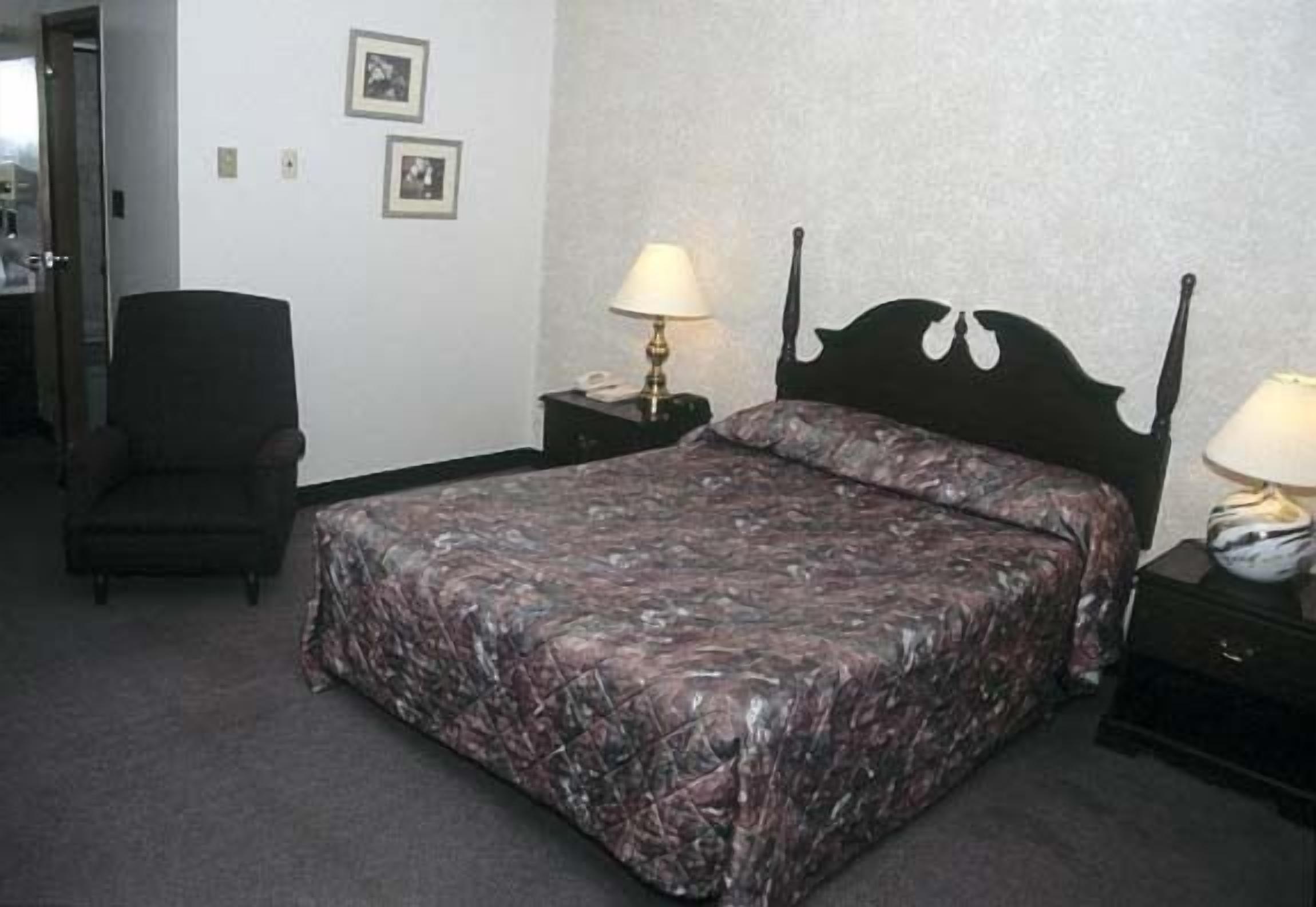 A standard hotel room with a bed, two bedside tables, a chair, and framed pictures on the wall.