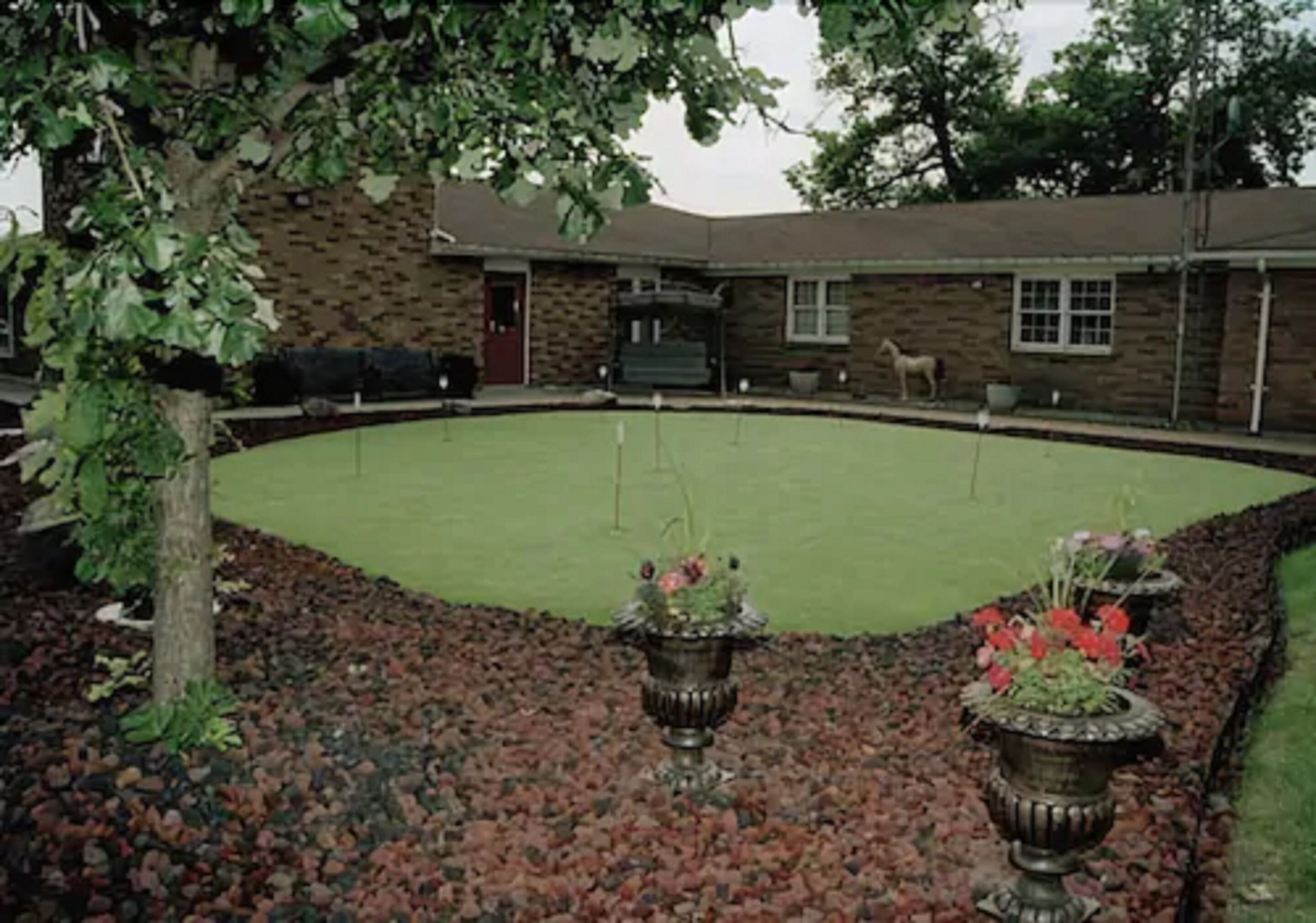 Un patio con césped verde, muros de piedra y jarrones decorativos.