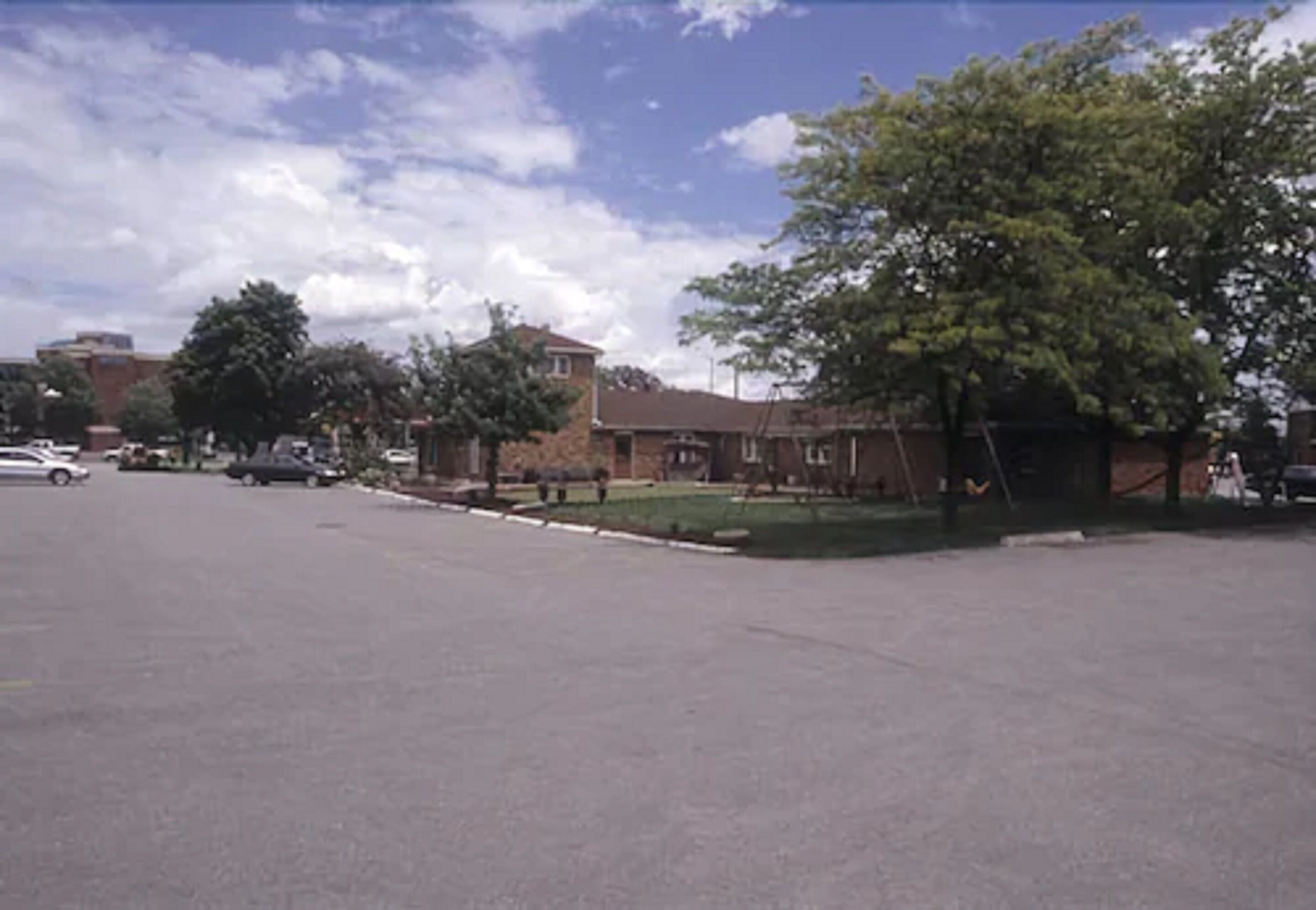 A parking lot with a few cars, a grassy area, and a building with a brick facade.