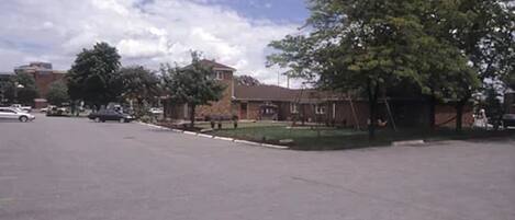 A parking lot with a few cars, a grassy area, and a building with a brick facade.