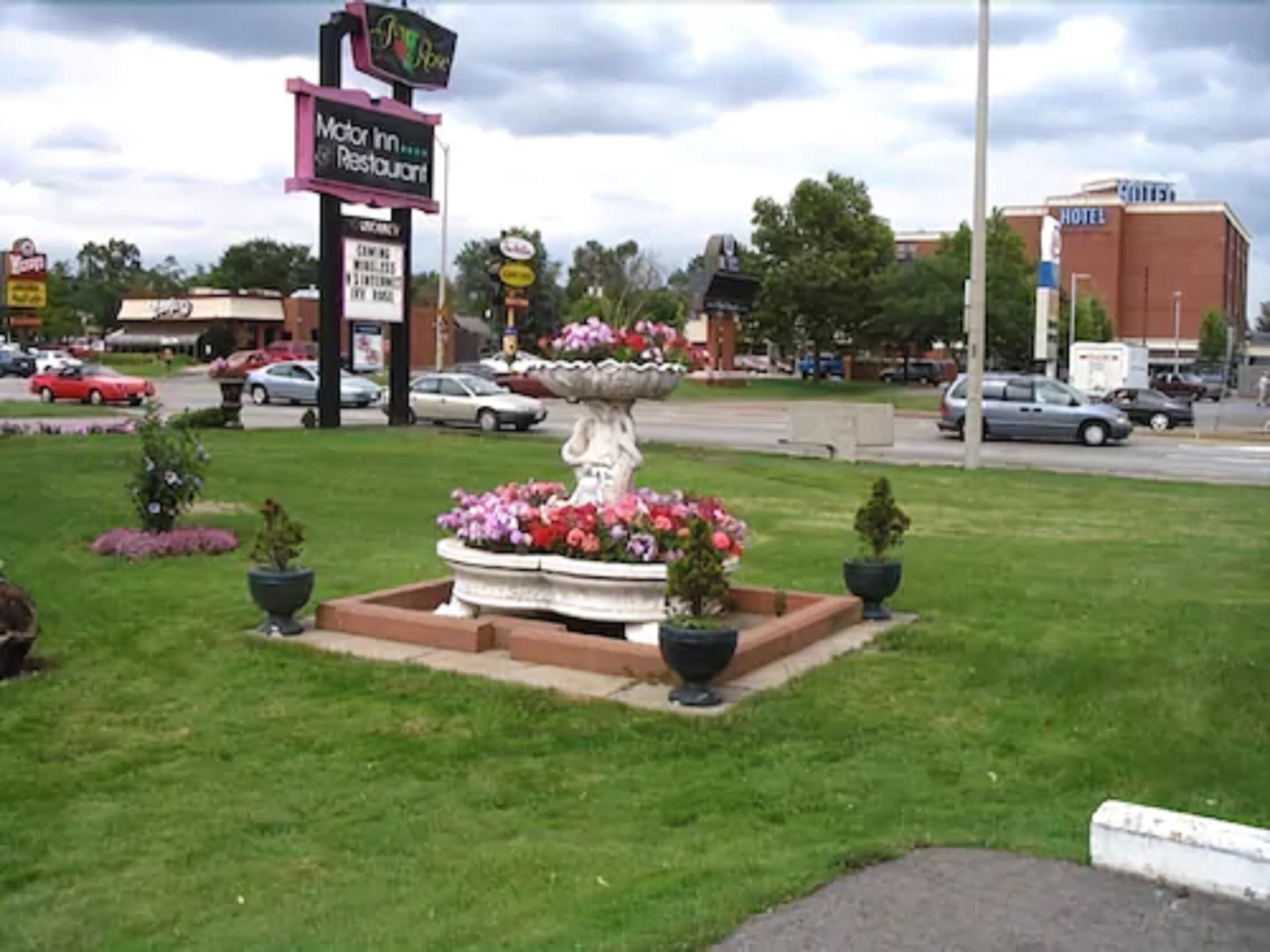 Señal de Motor Inn, una fuente con flores y un hotel al fondo.