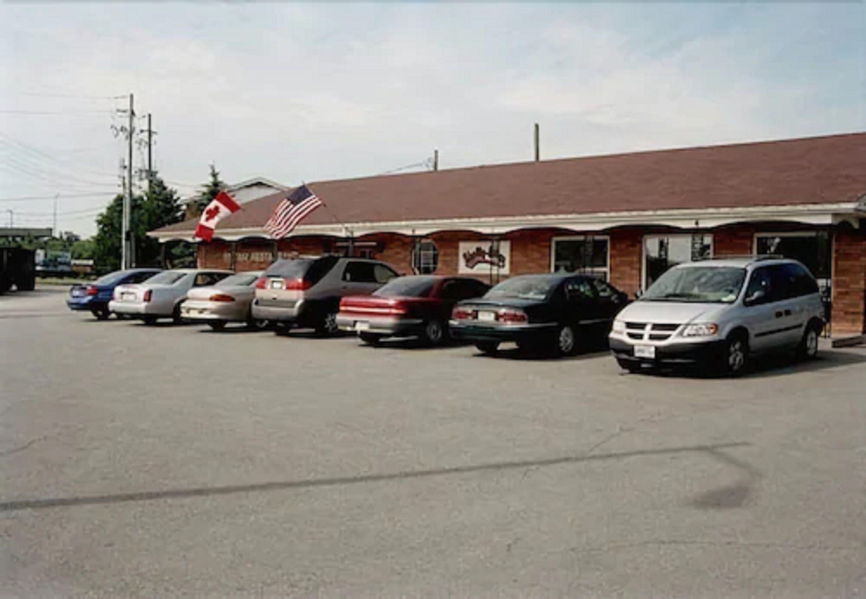 A parking lot with several cars parked in front of a building with a Canadian flag and an American flag.