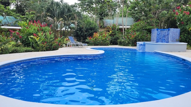 A swimming pool with a tiled edge, surrounded by lush greenery and a tiled deck. - Corinto Pearl Eco Resort (El Porvenir)