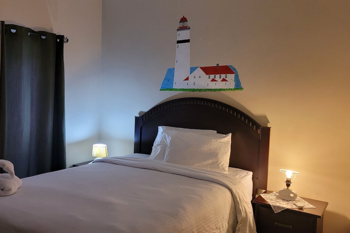 A neatly made bed with white linens, a dark wooden headboard, and a wall-mounted lamp on the nightstand.