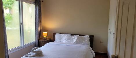 A hotel room with a bed, a nightstand, a lamp, and a window with curtains.