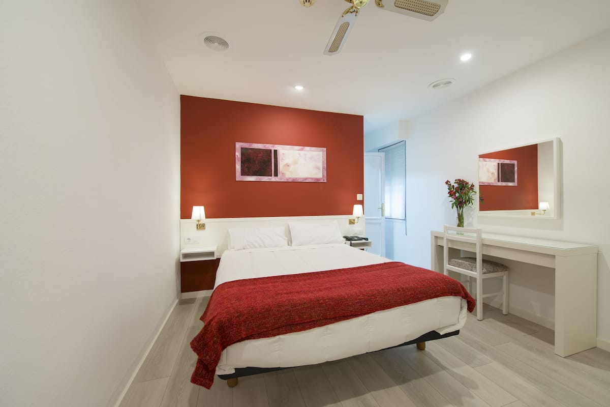A modern hotel room with a large bed, a desk, and a mirror.