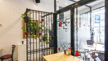 A modern cafe with a wooden table and metal chairs, a glass partition with red decorations, and a view of the street outside.