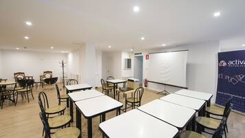 Een vergaderruimte met witte tafels en stoelen, een whiteboard en een projectiescherm.