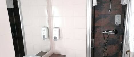Un baño moderno con cabina de ducha de vidrio, un lavamanos blanco y dos dispensadores de jabón para manos.