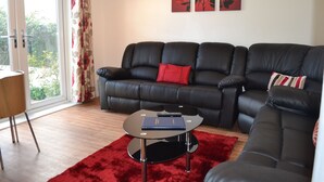 A modern living room with a black leather sofa, a red rug, and a glass coffee table. There are two red rose paintings on the wall. - Bristol Serviced Lettings - Filton (Bristol)