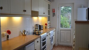 A kitchen with white cabinets, a wooden countertop, a stove, a washing machine, and a window with a view of greenery. - Bristol Serviced Lettings - Filton (Bristol)