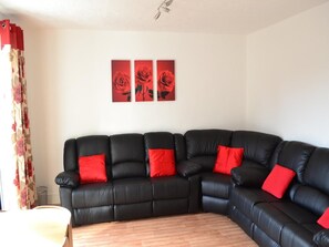 A black leather sectional sofa with red cushions, a wooden coffee table, and a wall with three red rose paintings. - Bristol Serviced Lettings - Filton (Bristol)