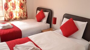 A hotel room with two beds, each with white bedding and red pillows. There are red towels on the beds and a red lamp on the nightstand. - Bristol Serviced Lettings - Filton (Bristol)