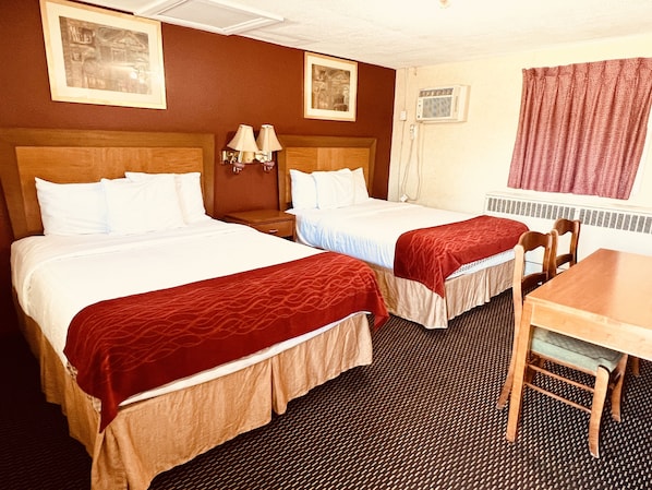 A hotel room with two beds, a small table, and a chair. There are two wall-mounted lamps and a window with curtains.