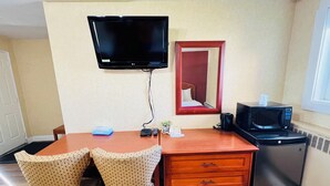 A hotel room with a wooden desk, two wicker chairs, a television mounted on the wall, a microwave, and a small refrigerator. - Bestway Motel (Windsor)