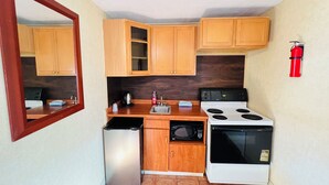 A compact kitchen with wooden cabinets, a stainless steel refrigerator, a microwave, a stove, and a sink. - Bestway Motel (Windsor)