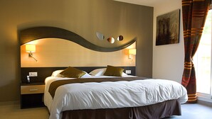 A modern hotel room with a large bed, two bedside tables, a wall-mounted lamp, and a painting.