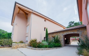 A two-story building with a stone facade and a pink exterior. There is a stone archway leading to a covered entrance. - The Originals City, Hôtel Les Bastides du Gapeau, Hyères Nord (Sollies-Toucas)