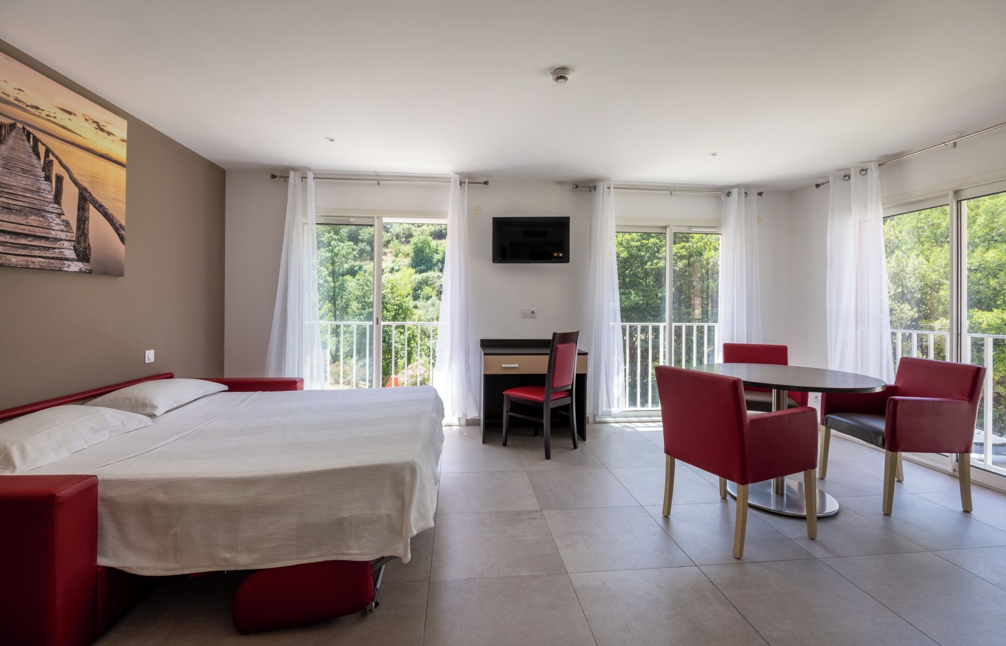 Quarto de hotel com cama, escrivaninha, cadeira, mesa e televisão.