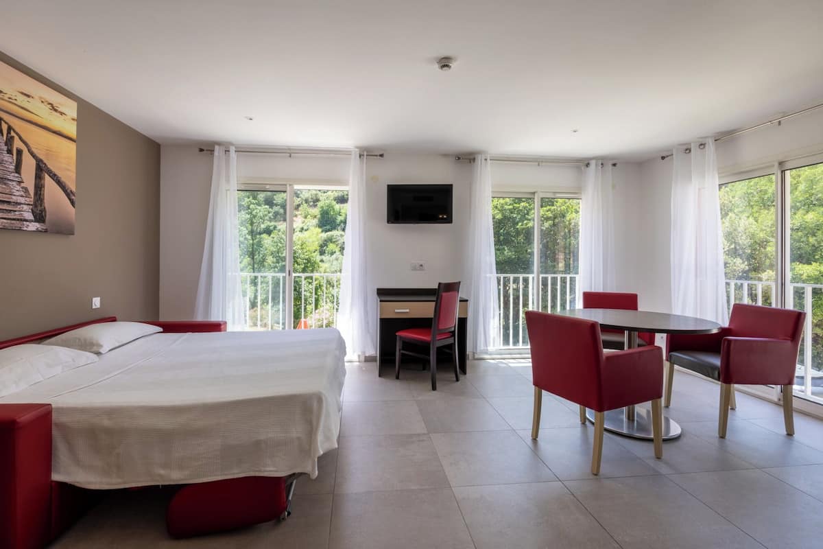 Quarto de hotel com cama, escrivaninha, cadeira, mesa e televisão.