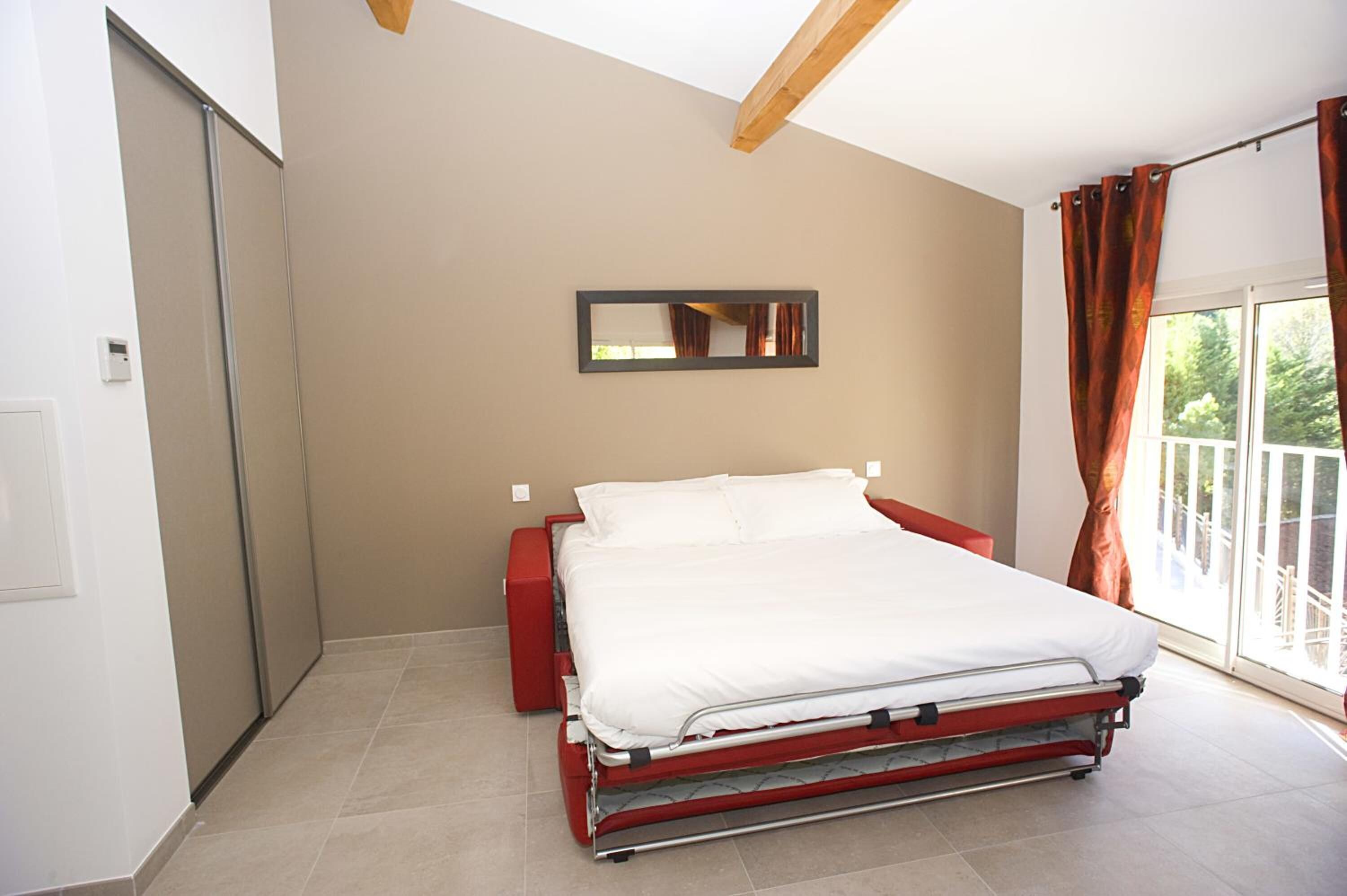 Ein Schlafzimmer mit Bett, Nachttisch, Spiegel und einem Fenster mit Vorhängen.
