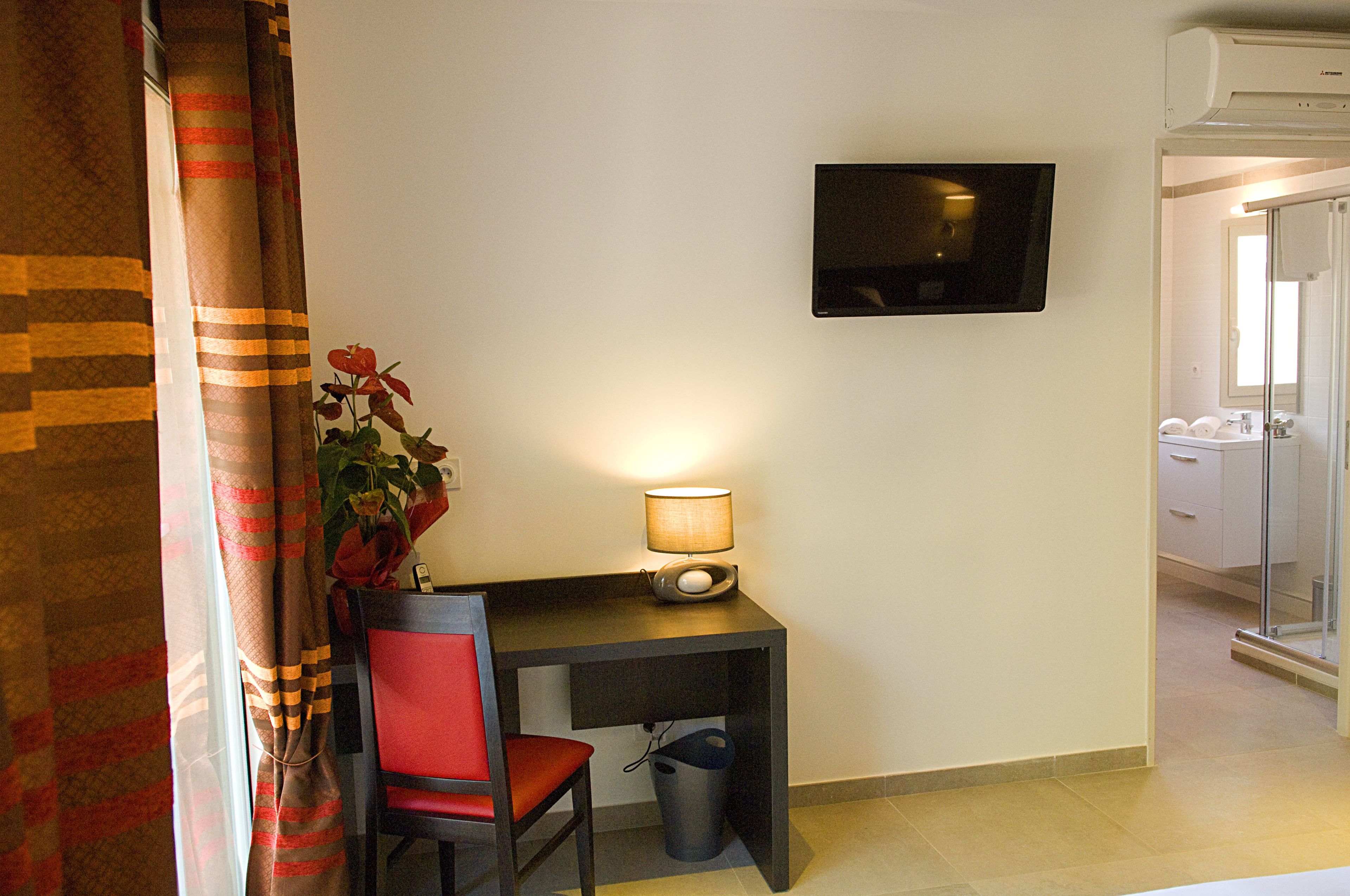 Habitación de hotel con escritorio, silla, televisión y planta en maceta.