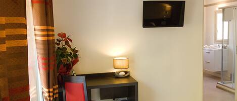 Habitación de hotel con escritorio, silla, televisión y planta en maceta.
