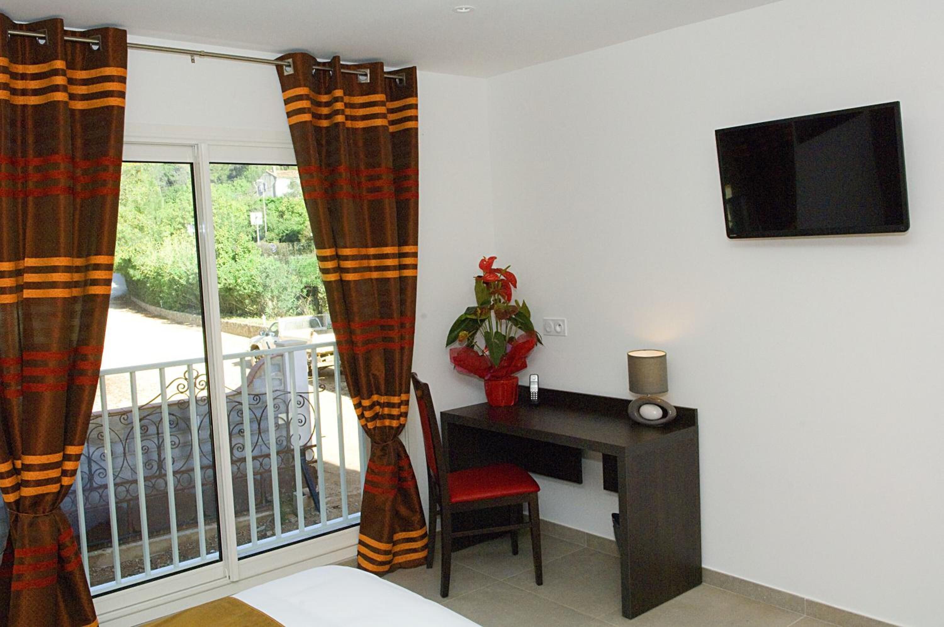 A room with a bed, a desk with a chair, a TV on the wall, and a window with curtains.