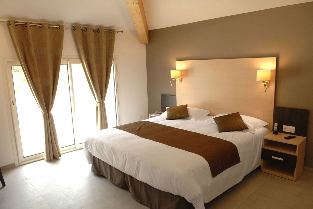 Un dormitorio con una cama grande, dos lámparas de noche, una mesita de noche y una ventana con cortinas.
