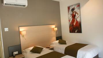 A hotel room with two beds, a headboard with wall-mounted lamps, an air conditioner, and a painting on the wall.