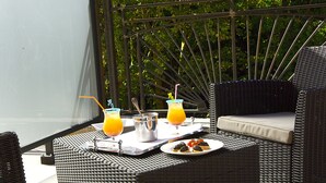 An outdoor dining area with wicker furniture, a metal railing, and a view of trees.