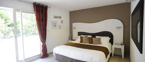 Habitación de hotel con una cama grande, una mesita de noche, un televisor montado en la pared y una puerta corrediza de vidrio al exterior.