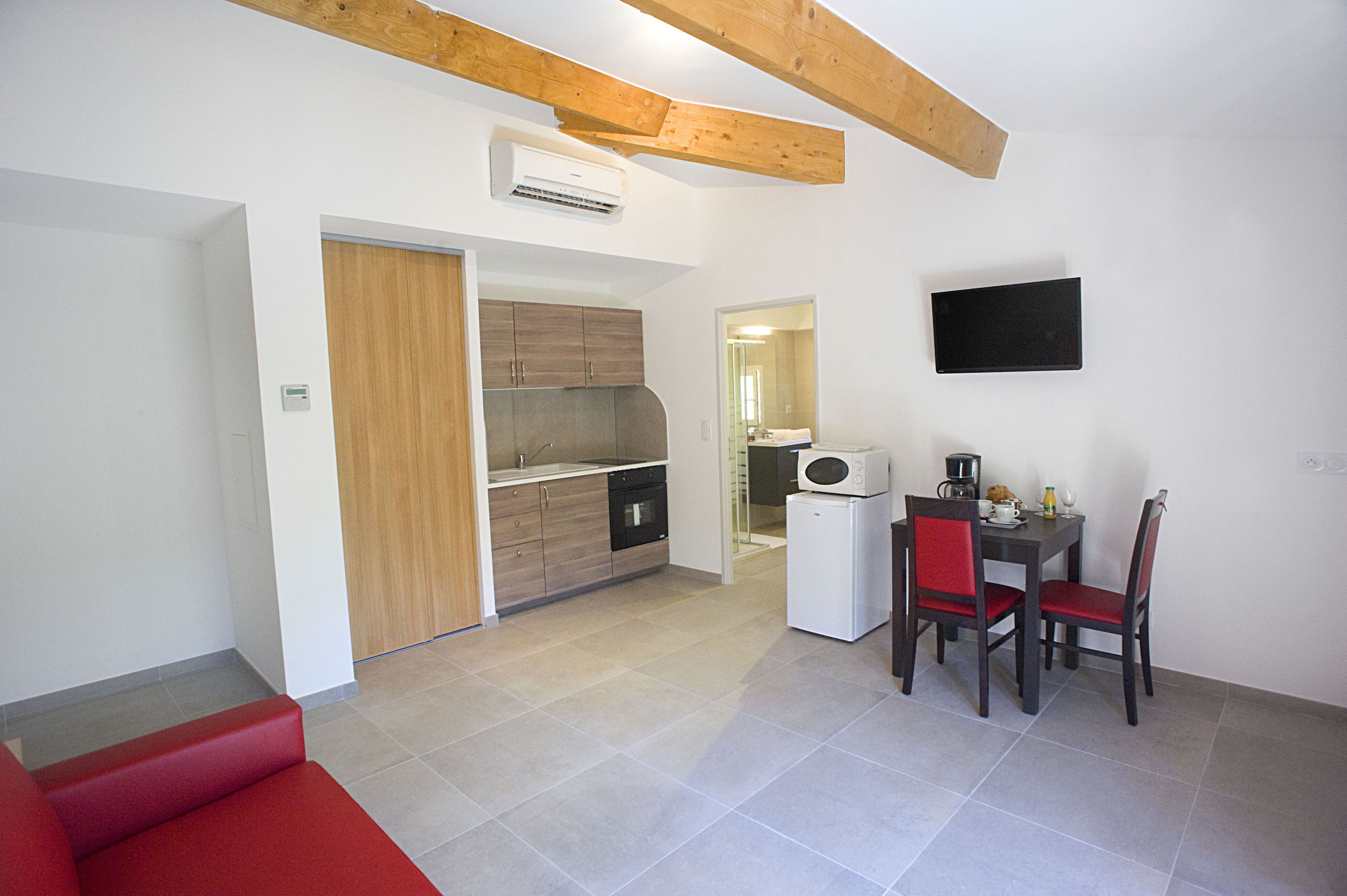 A compact living space with a kitchenette, a dining area with a table and chairs, and a red sofa.