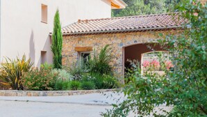 A stone building with a tiled roof, surrounded by various plants and a stone wall.