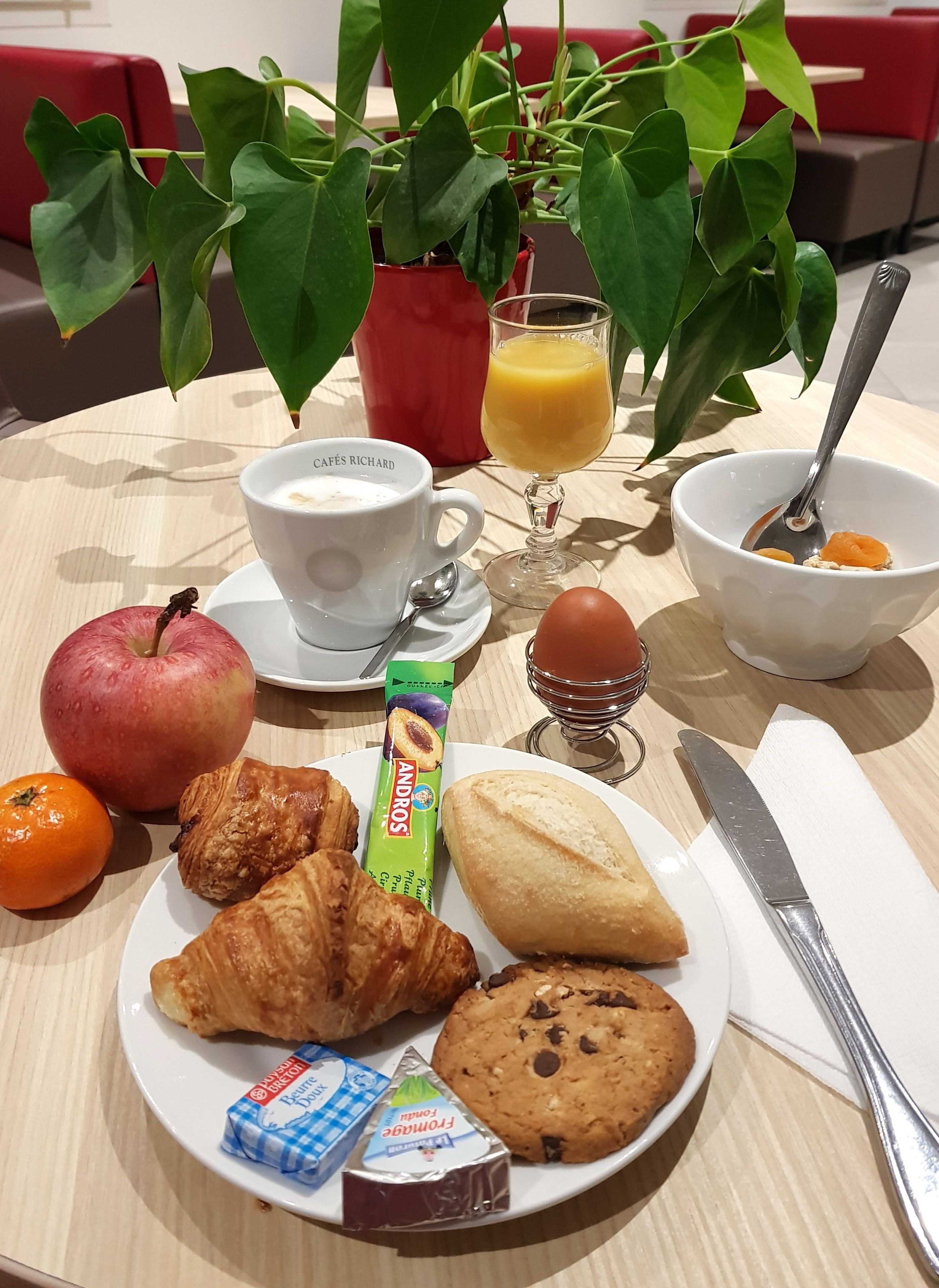 A breakfast setting with a croissant, apple, orange, and a plate with a cookie and chocolate bar.