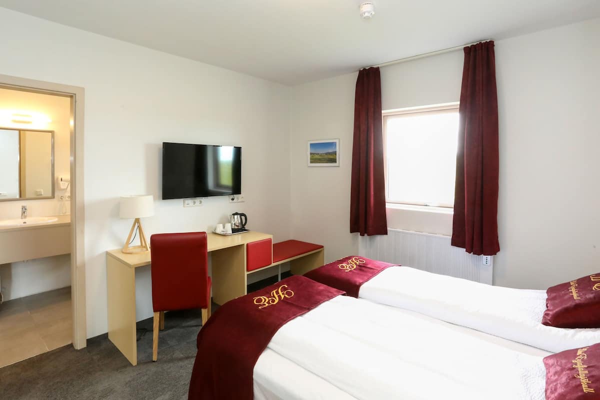 Ein Hotelzimmer mit einem Bett, einem Schreibtisch mit Stuhl, einem Fernseher, einem Fenster mit Vorhängen, einem Waschbecken und einem Spiegel.