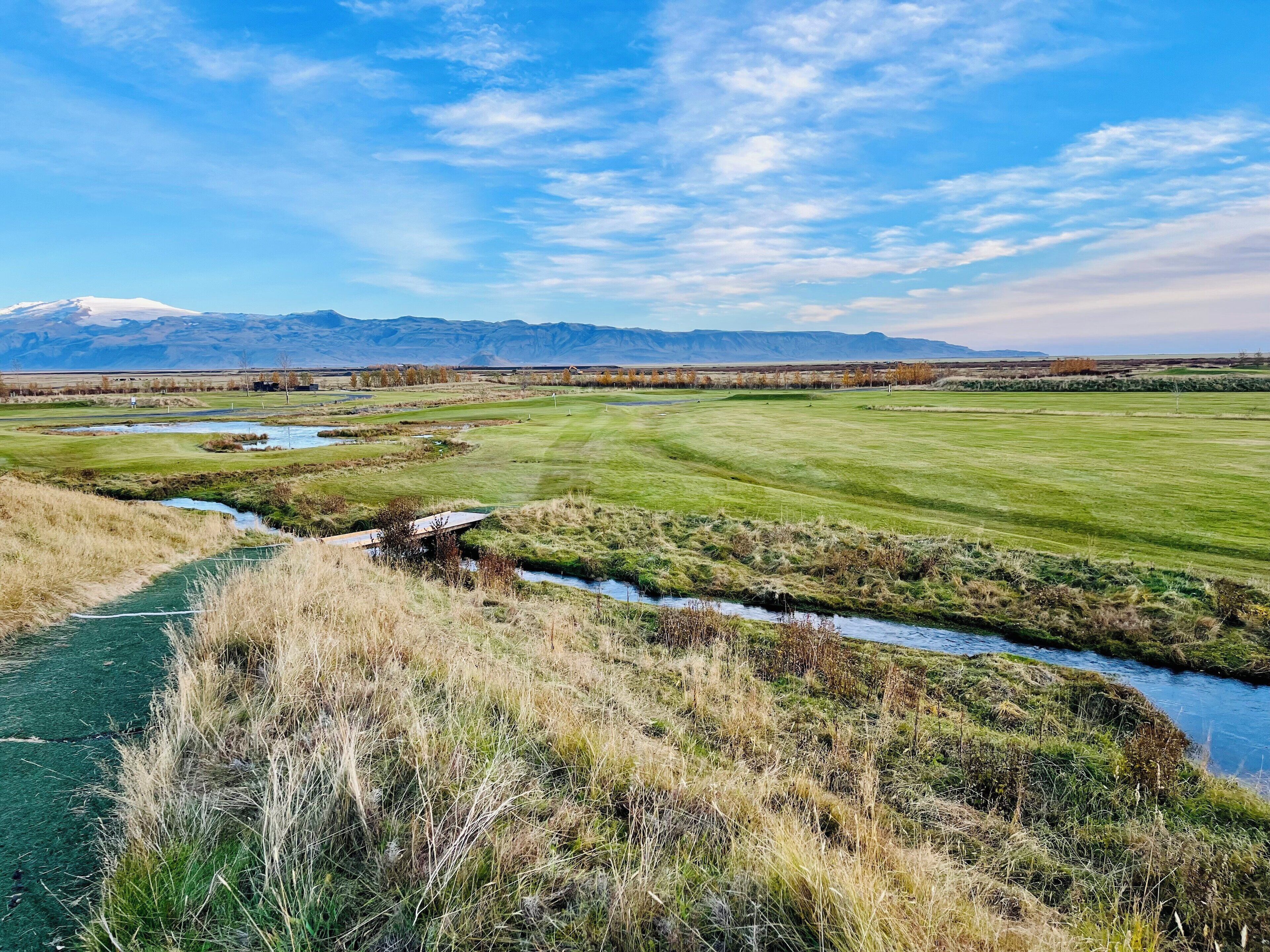 A golf course with a river, a bridge, and mountains in the background.