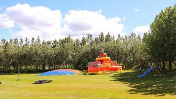 Kids can play on the inflatable play structure and enjoy the slides in this outdoor recreational area surrounded by a grassy field and trees.