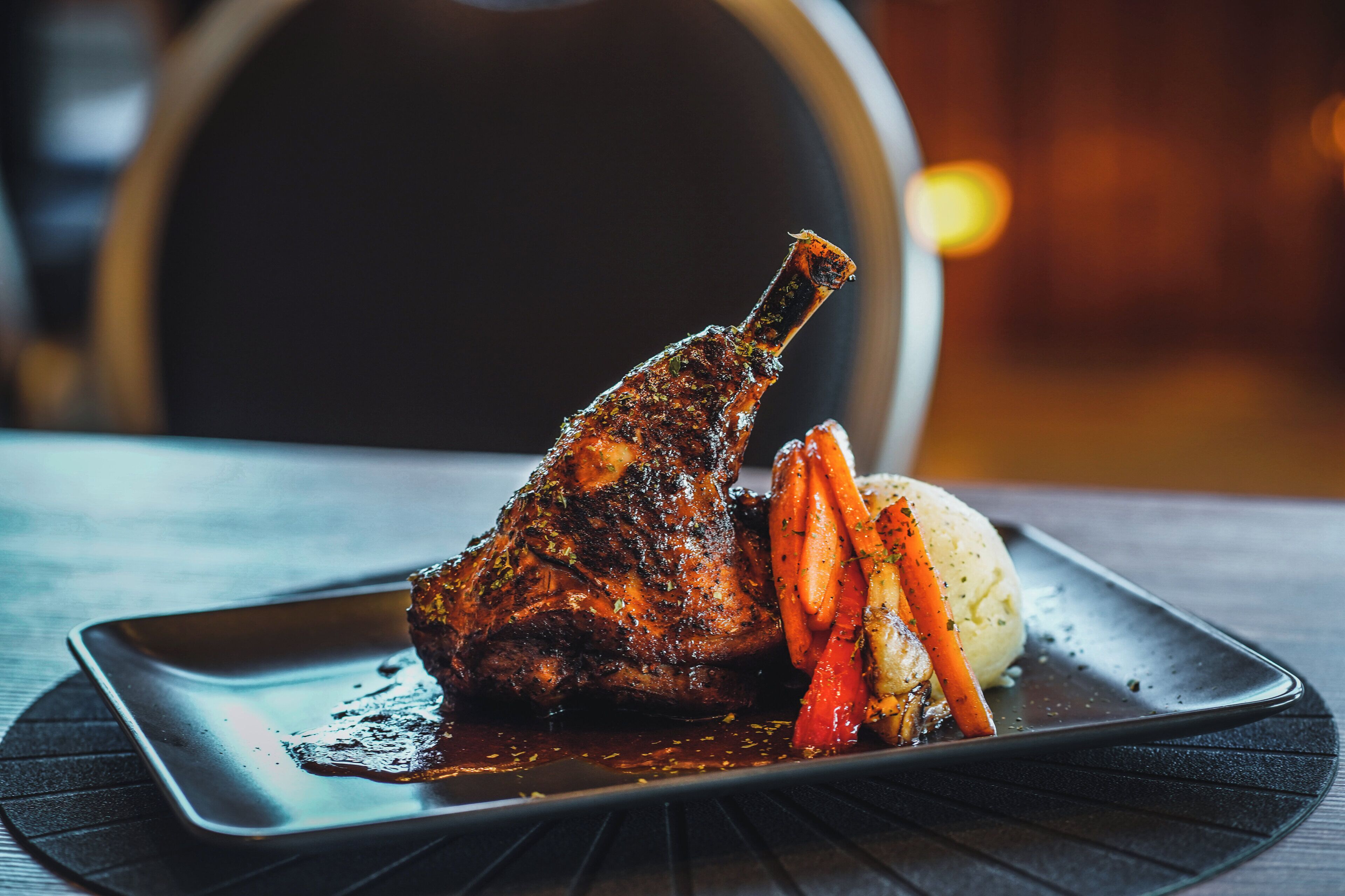A plate with a roasted lamb leg, carrots, and a potato.